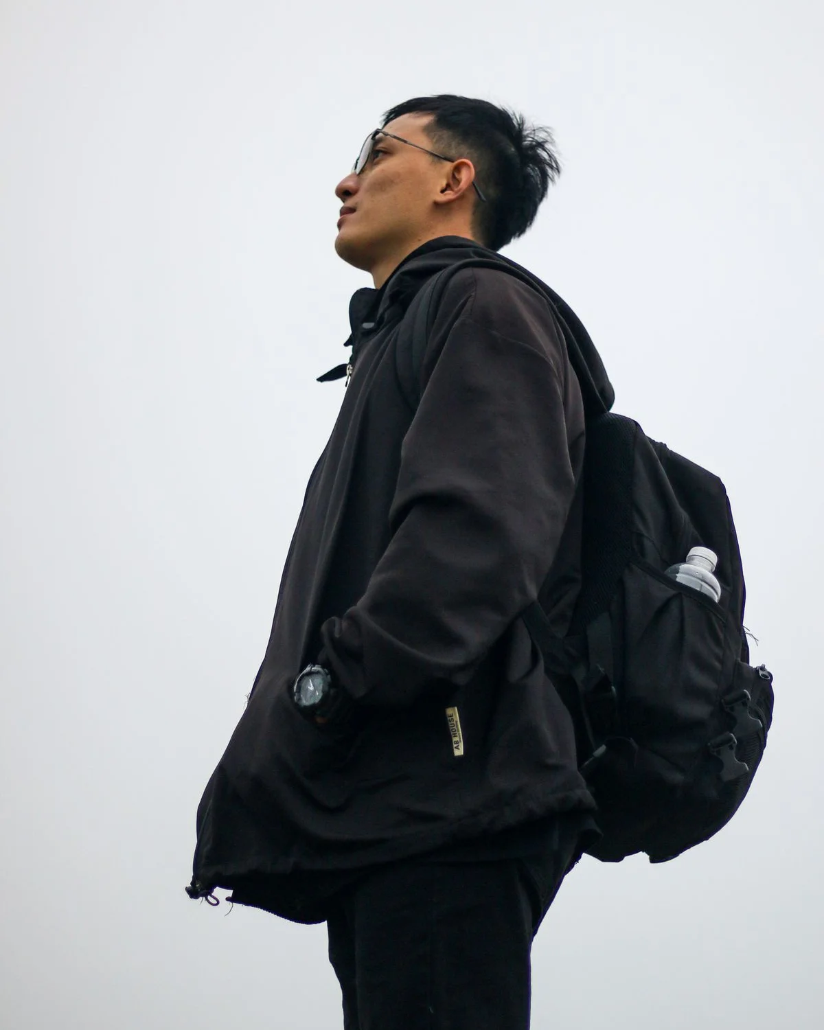 Black hooded outdoor jacket worn with a backpack against an overcast sky